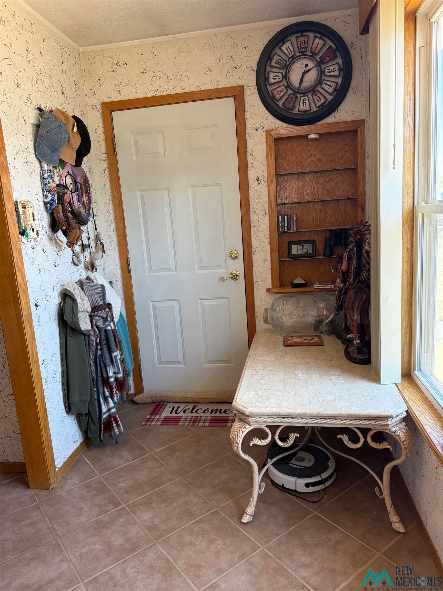 4010 540th Loop Logan, NM 88426 - Photo 22 of 38 Neutral tone tile flooring featuring a white panel door with wood trim, a built-in wooden shelving unit, and a window with wood-finish casing