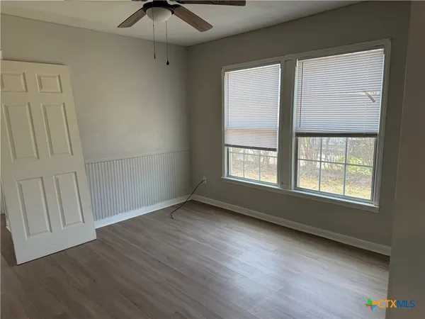 an empty room with wooden floor fan and windows