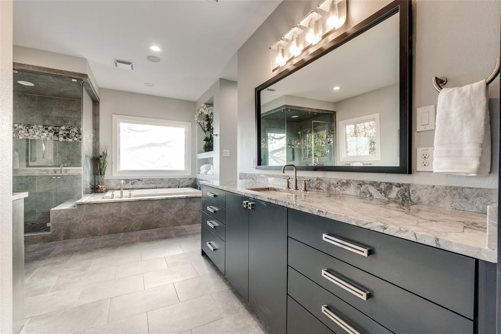 7912 Hanover Street Dallas, TX 75225 - Photo 8 of 29 Large bathroom featuring a dual vanity with a light-toned countertop, a large framed mirror, a built-in soaking tub, a separate glass-enclosed shower, and light gray tile flooring