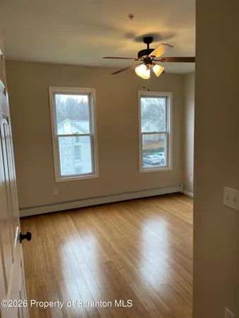 an empty room with wooden floor chandelier fan and windows