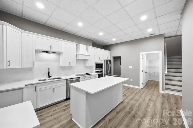 a large white kitchen with a stove a sink dishwasher and a refrigerator with wooden floor