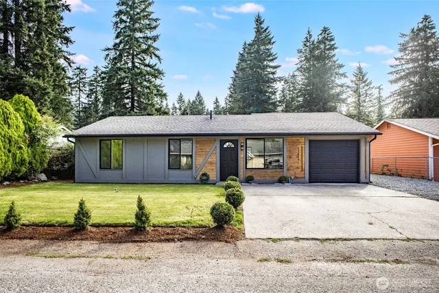 a view of a house with a yard plants and large tree