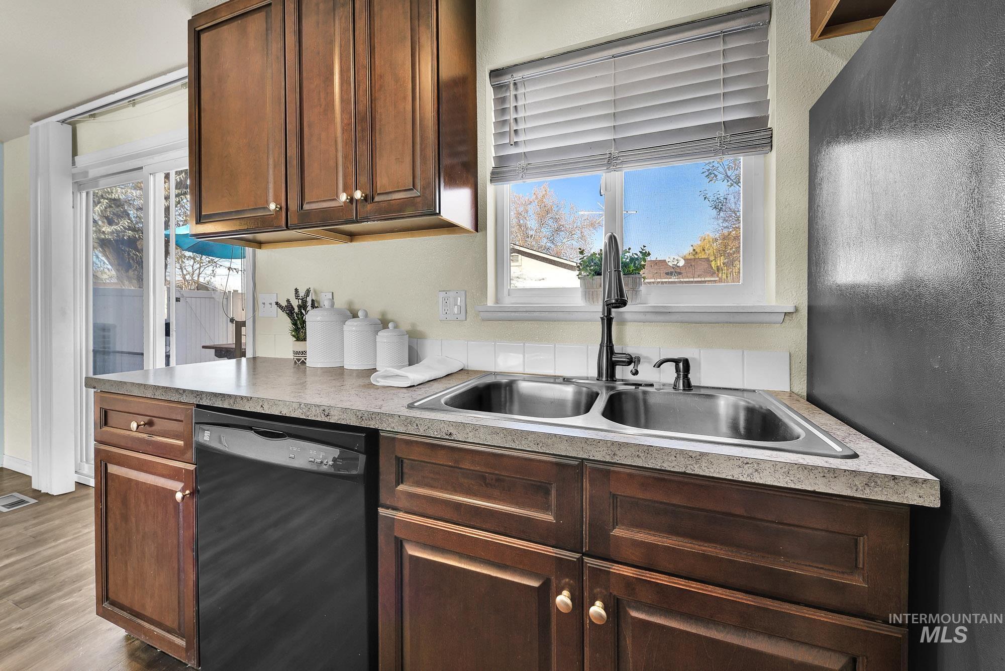 901 East 2nd Street South Middleton, ID 83644 - Photo 12 of 50 Kitchen with black dishwasher, light granite look countertops, stainless steel sink with window above, laminate wood-style flooring, and plenty of natural light