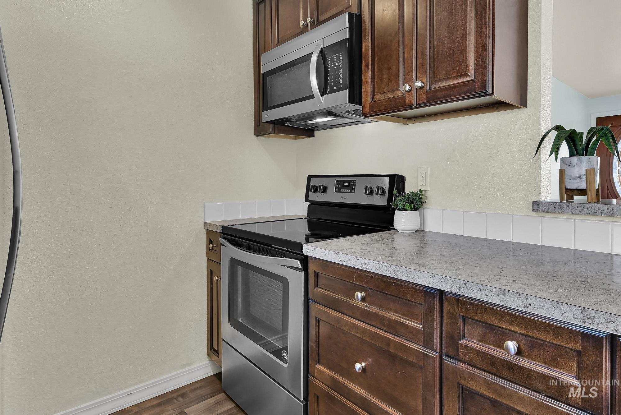 901 East 2nd Street South Middleton, ID 83644 - Photo 13 of 50 Kitchen with rich brown cabinetry, appliances with stainless steel finishes, light granite style countertops, laminate wood-type flooring, and a textured wall