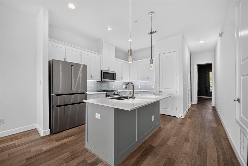 5015 Meridian Lane, Unit 2102 Addison, TX 75001 - Photo 10 of 36 Modern kitchen featuring white cabinetry, stainless steel appliances, a center island with a sink, pendant lighting, and wood-finish flooring