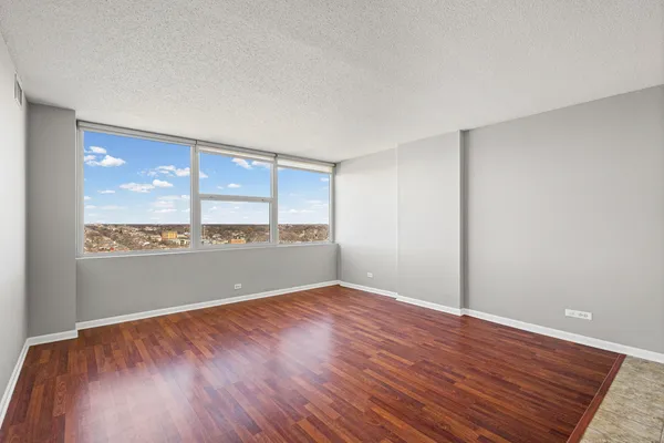 a view of an empty room with wooden floor and a window