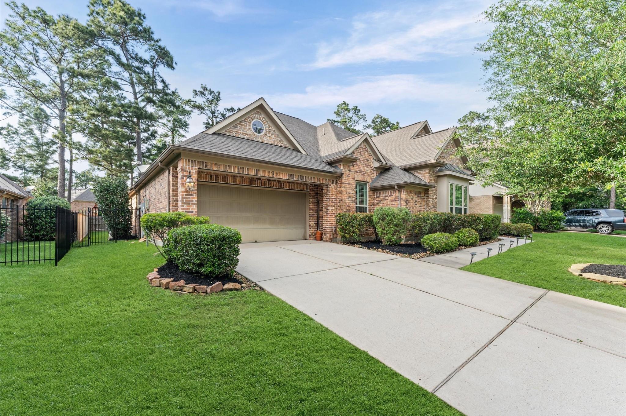 70 Valera Ridge Drive Spring, TX 77389 - Photo 33 of 37 This photo shows a charming brick home with a well-maintained front yard and a spacious driveway leading to a two-car garage. The property is surrounded by mature trees and neatly trimmed bushes, providing a serene and inviting atmosphere.