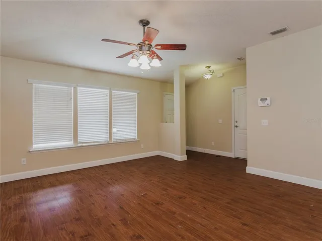 an empty room with wooden floor chandelier fan and windows