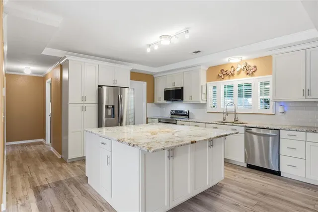 a kitchen with stainless steel appliances granite countertop a refrigerator a sink dishwasher a oven with white cabinets and wooden floor