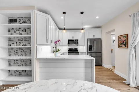 a kitchen with stainless steel appliances kitchen island granite countertop a refrigerator a stove and white cabinets with wooden floor