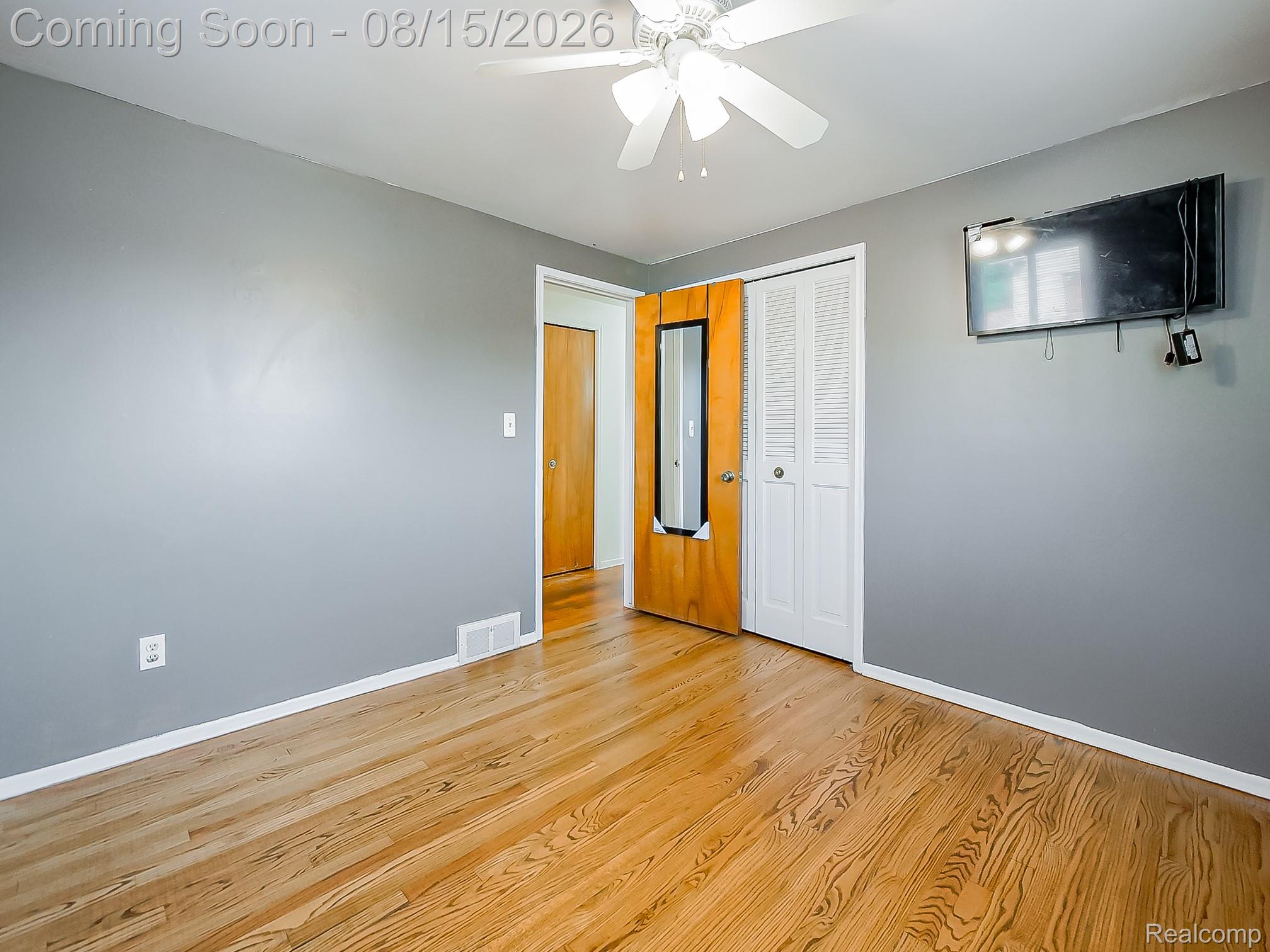 21131 Harvard Road Southfield, MI 48076 - Photo 20 of 33 Spacious bedroom featuring warm wood-finish flooring, soft gray walls, ceiling fan with integrated lighting, and dual closet access including a mirrored door