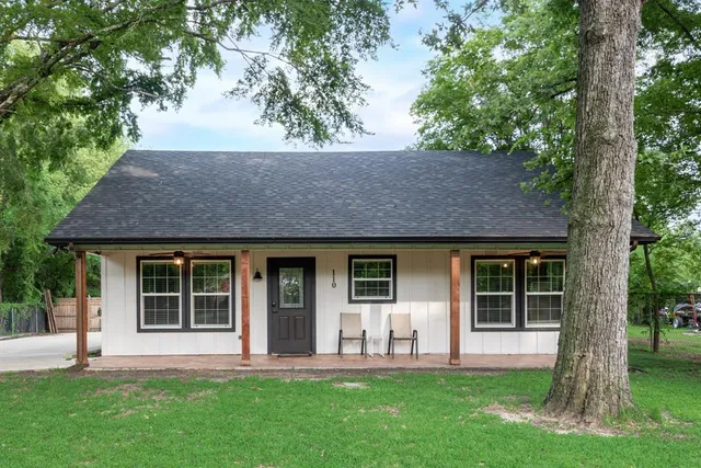 a front view of a house with a yard and a large tree