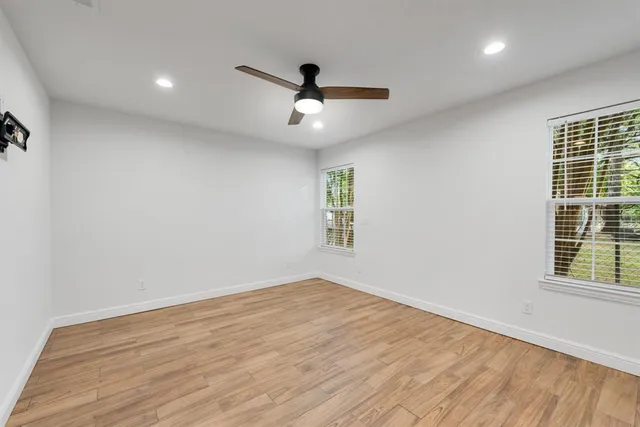 an empty room with wooden floor ceiling fan and windows