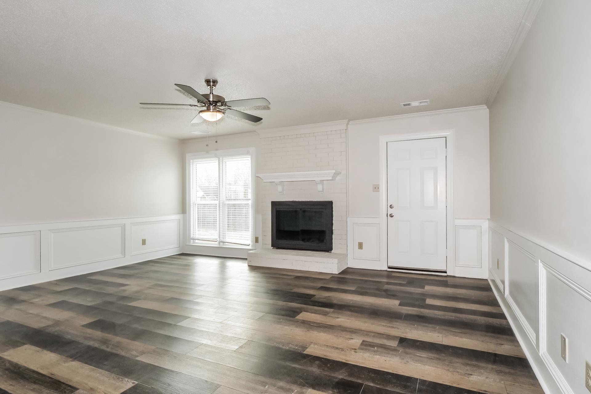 675 South Collierville Arlington Road Collierville, TN 38017 - Photo 2 of 17 Unfurnished living room featuring a decorative wall, a wainscoted wall, a ceiling fan, a brick fireplace, and dark wood-type flooring