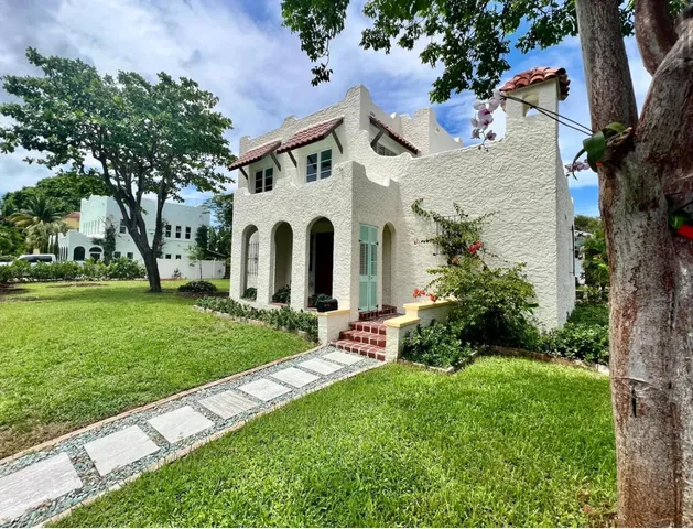 a view of a white house with a small yard and large trees