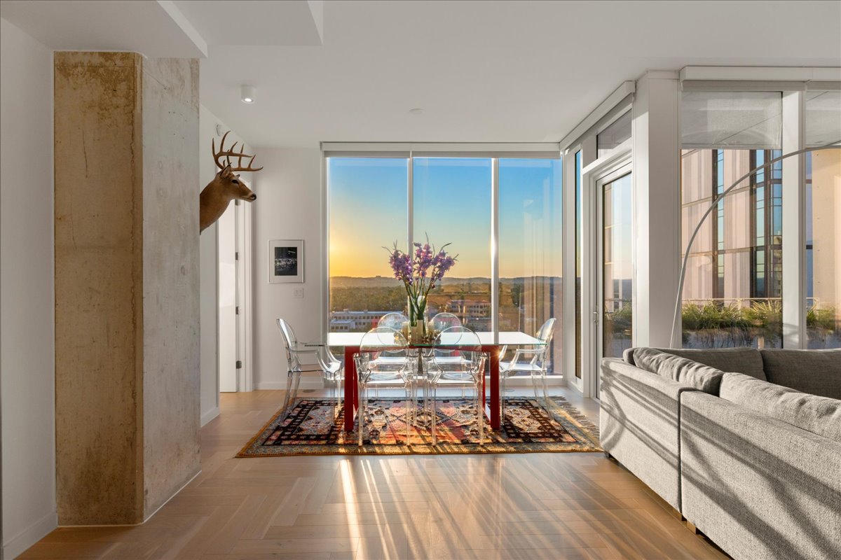 313 West 17th Street, Unit 1104 Austin, TX 78701 - Photo 4 of 40 A sun-soaked dining area wrapped in floor-to-ceiling glass, capturing uninterrupted Hill Country and sunset views. The herringbone wood floors and open layout create a gallery-like setting for intimate meals or chef-led Omakase dinners, with golden hour light transforming the space each evening.