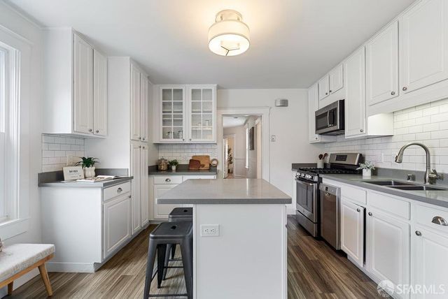 a kitchen with stainless steel appliances granite countertop a refrigerator a stove top oven a sink dishwasher and white cabinets with wooden floor