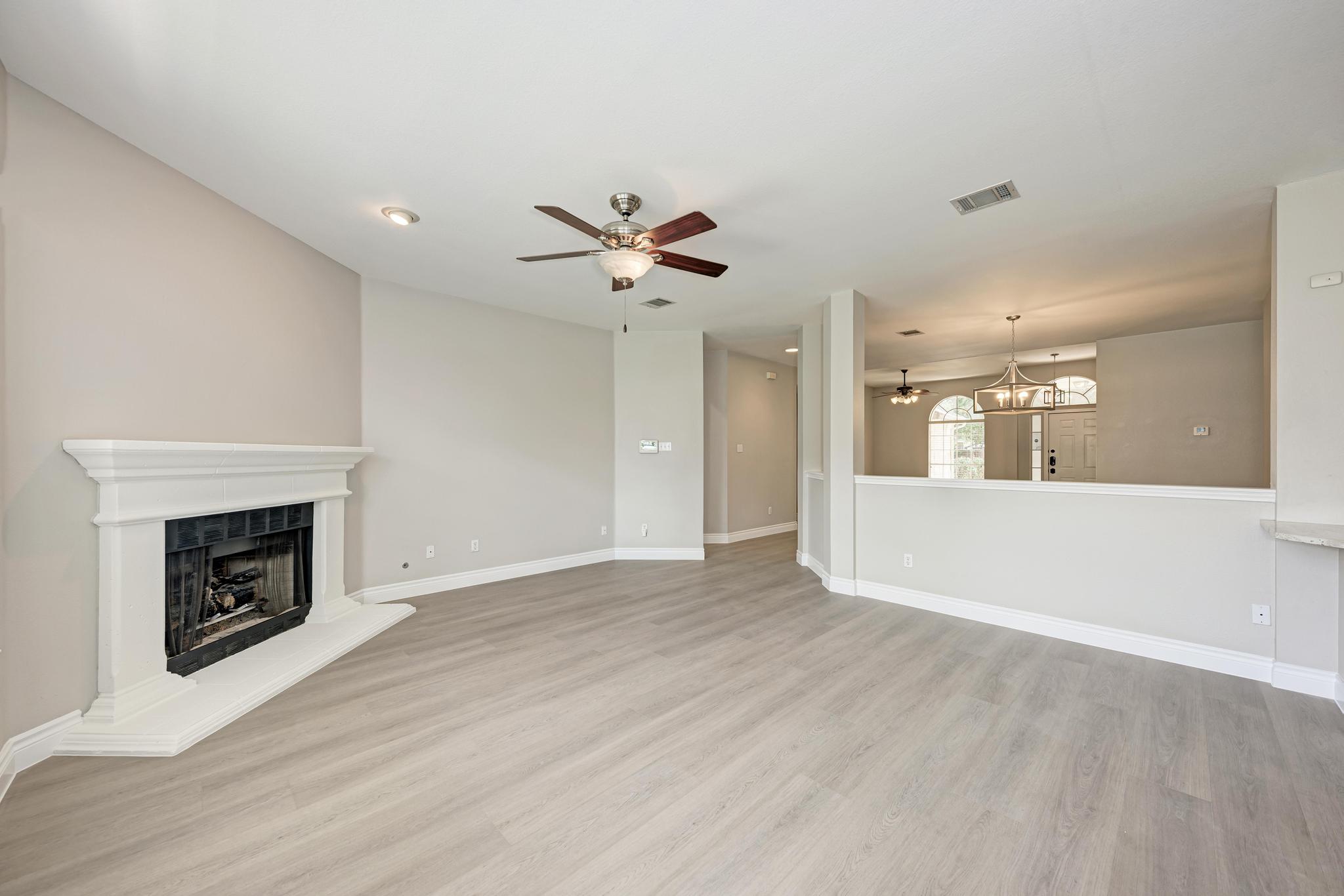 4408 Tello Path Austin, TX 78749 - Photo 10 of 38 Unfurnished living room featuring a ceiling fan, wood finished floors, a fireplace with raised hearth, and a chandelier