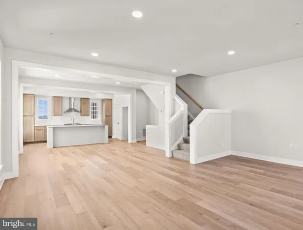 a view of an empty room with wooden floor and a kitchen