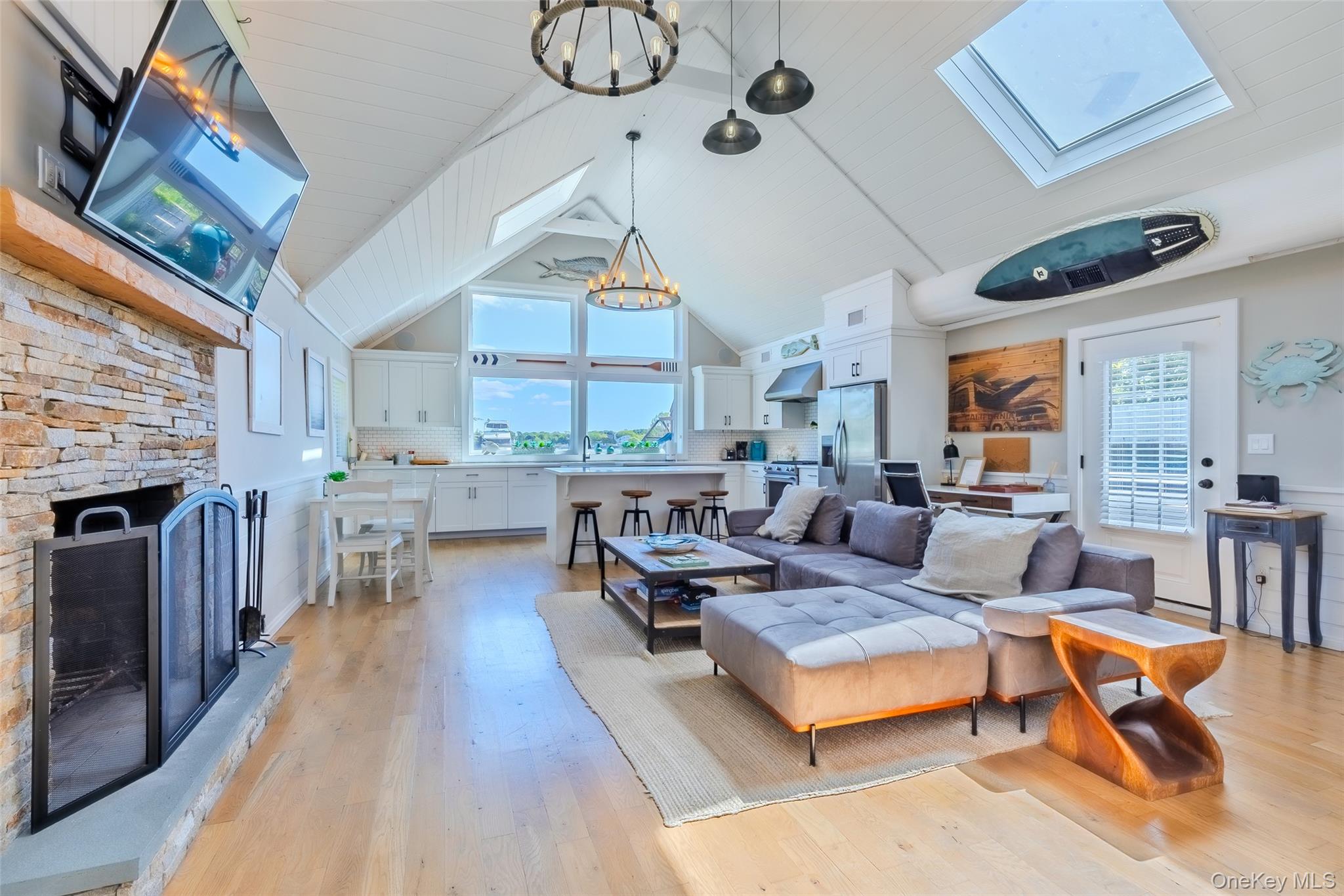 53 Old Neck Road South Center Moriches, NY 11934 - Photo 19 of 50 Living room with a fireplace, light wood-style floors, a chandelier, a skylight, and high vaulted ceiling