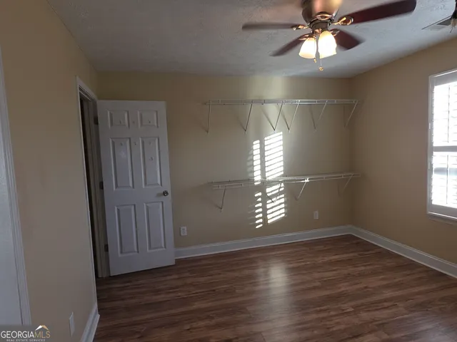 an empty room with wooden floor chandelier fan and windows