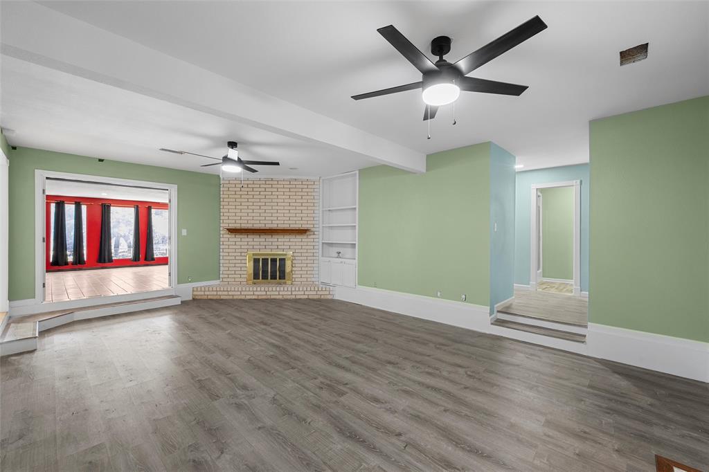 544 Lusk Creek Road Eddy, TX 76524 - Photo 5 of 39 Unfurnished living room featuring a ceiling fan, wood finished floors, a brick fireplace, built in shelves, and beamed ceiling