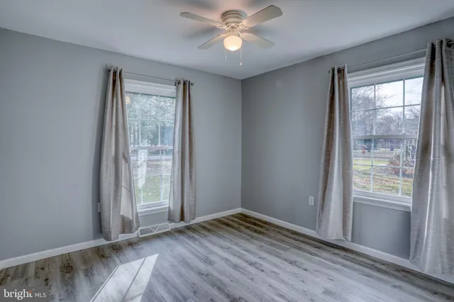 an empty room with wooden floor fan and windows