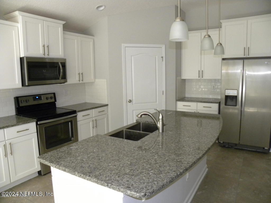a kitchen with stainless steel appliances granite countertop a sink a microwave a refrigerator and white cabinets