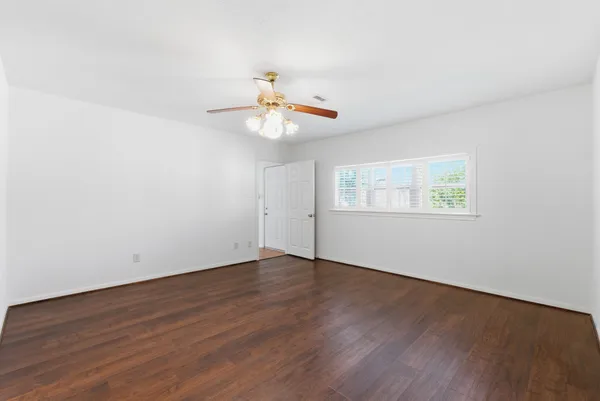 an empty room with wooden floor chandelier fan and windows