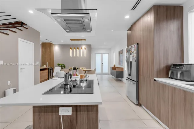 a kitchen with stainless steel appliances kitchen island granite countertop a dining table chairs and a refrigerator