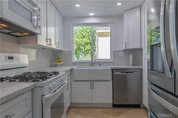 a kitchen with granite countertop white cabinets appliances and a window