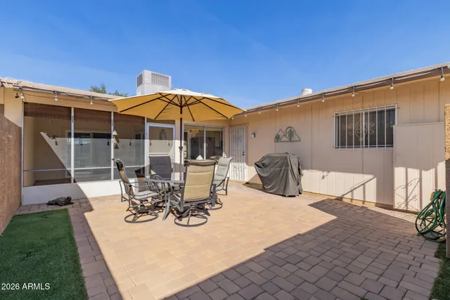 a view of a patio with table and chairs under an umbrella with a barbeque grill and plants