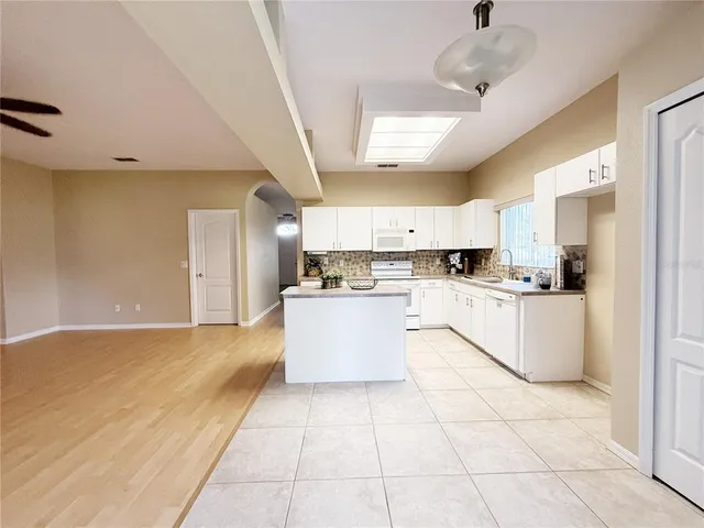 a large kitchen with stainless steel appliances granite countertop a stove a sink a refrigerator white cabinets and couches with wooden floor