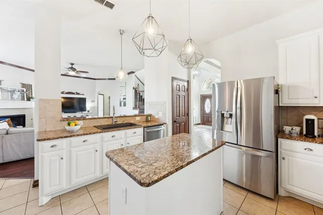 a kitchen with granite countertop stainless steel appliances a refrigerator a sink and white cabinets