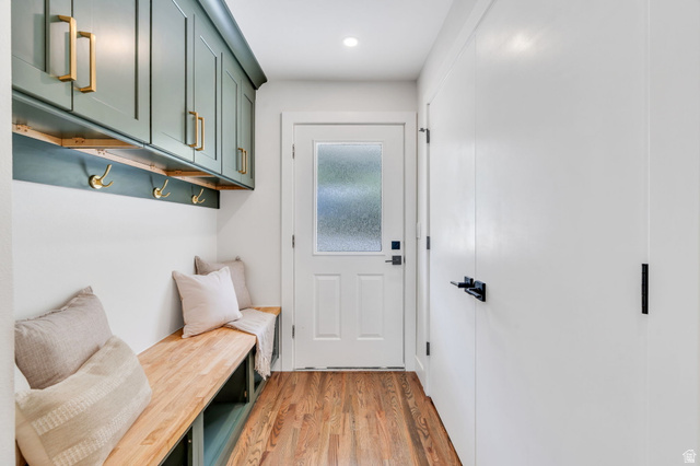 3813 North Foothill Drive Provo, UT 84604 - Photo 45 of 71 Entryway mudroom featuring wood-finish flooring, built-in bench seating, overhead cabinetry, wall-mounted hooks, and a white door with frosted glass