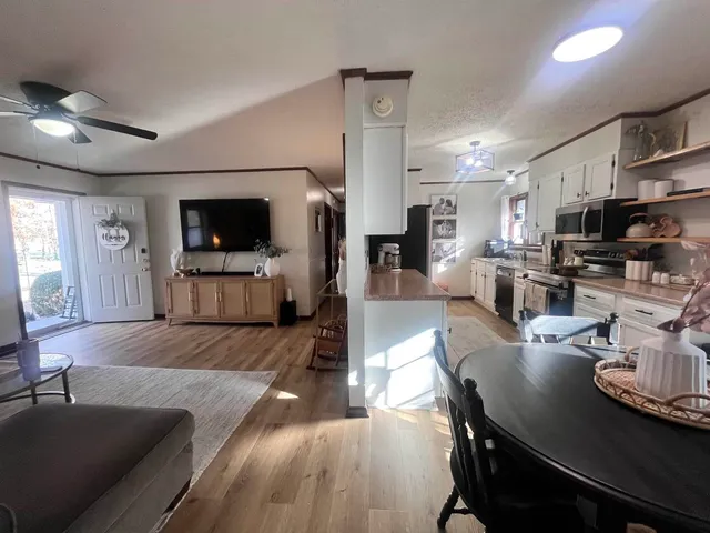 a living room with stainless steel appliances a dining table a flat screen tv and kitchen view