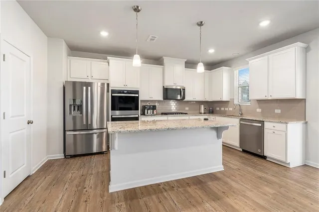 a kitchen with stainless steel appliances granite countertop a refrigerator a stove a sink and white cabinets with wooden floor