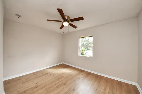 an empty room with wooden floor ceiling fan and windows