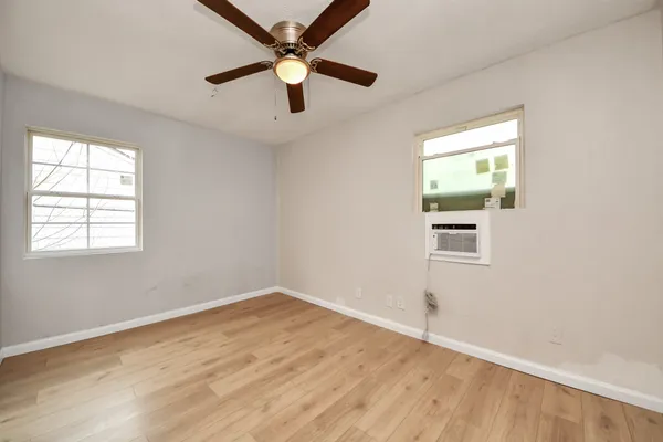 an empty room with wooden floor fan and windows