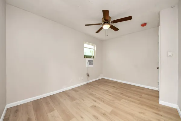 a view of an empty room with wooden floor and a ceiling fan