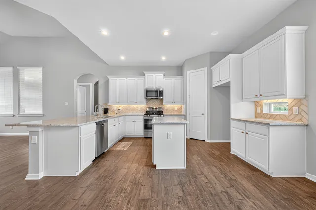 a kitchen with stainless steel appliances granite countertop a sink a stove top oven and white wooden cabinets