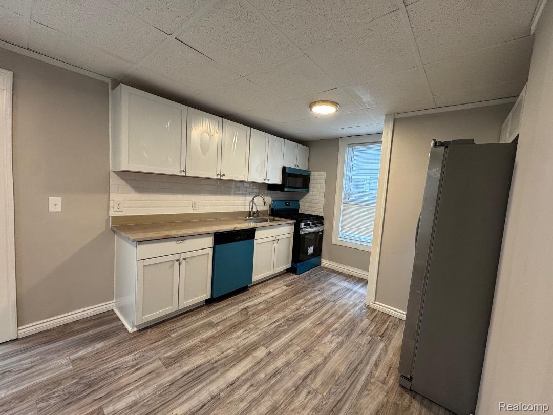 8220 Hudson Avenue Warren, MI 48089 - Photo 13 of 28 Kitchen featuring black appliances, backsplash, white cabinets, light wood finished floors, and a paneled ceiling
