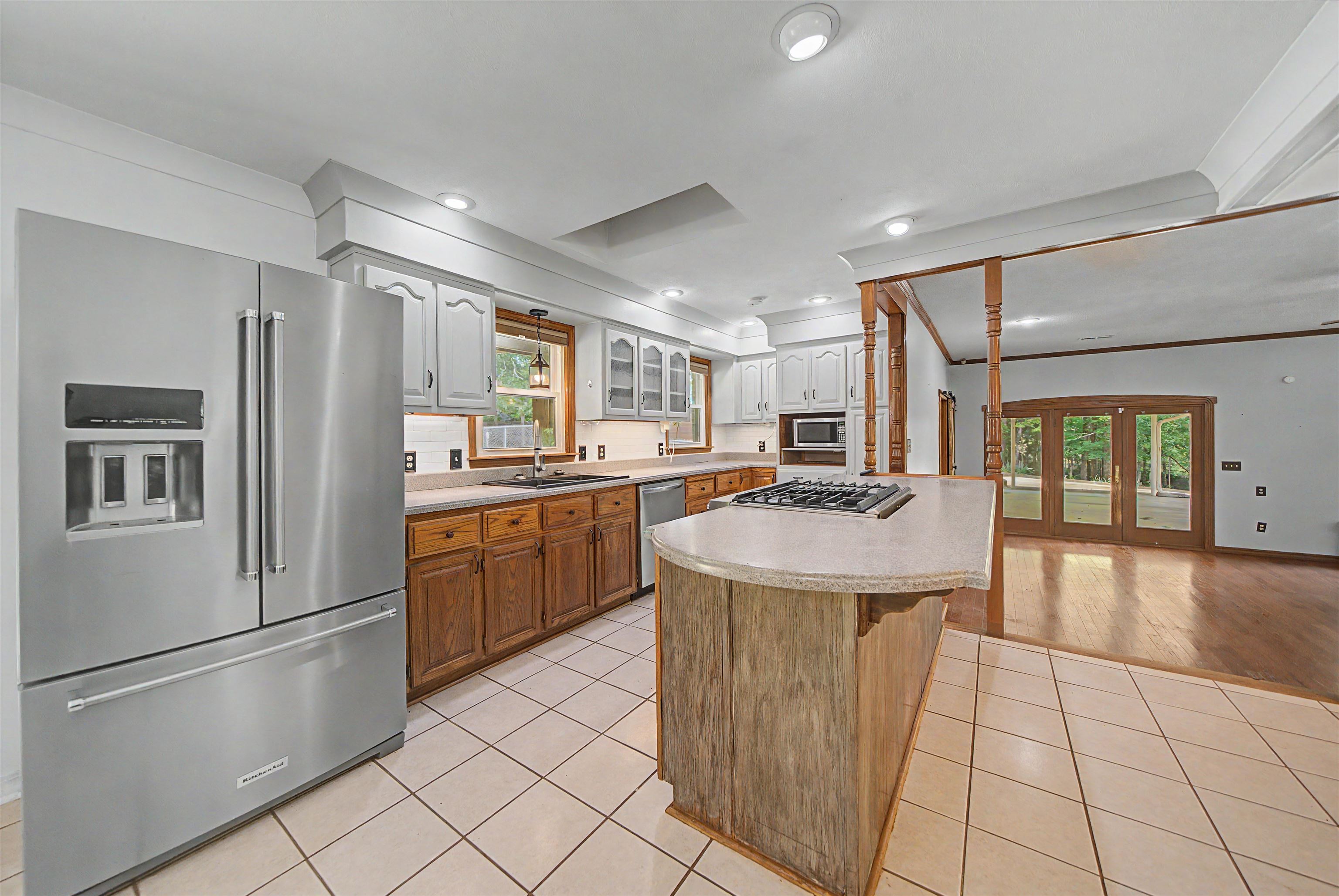 436 Skyline Road Selmer, TN 38375 - Photo 36 of 40 Kitchen featuring a stainless steel French-door refrigerator, gas cooktop on an island with a light-toned countertop, white upper cabinetry, wood-finish lower cabinetry, and white tile flooring