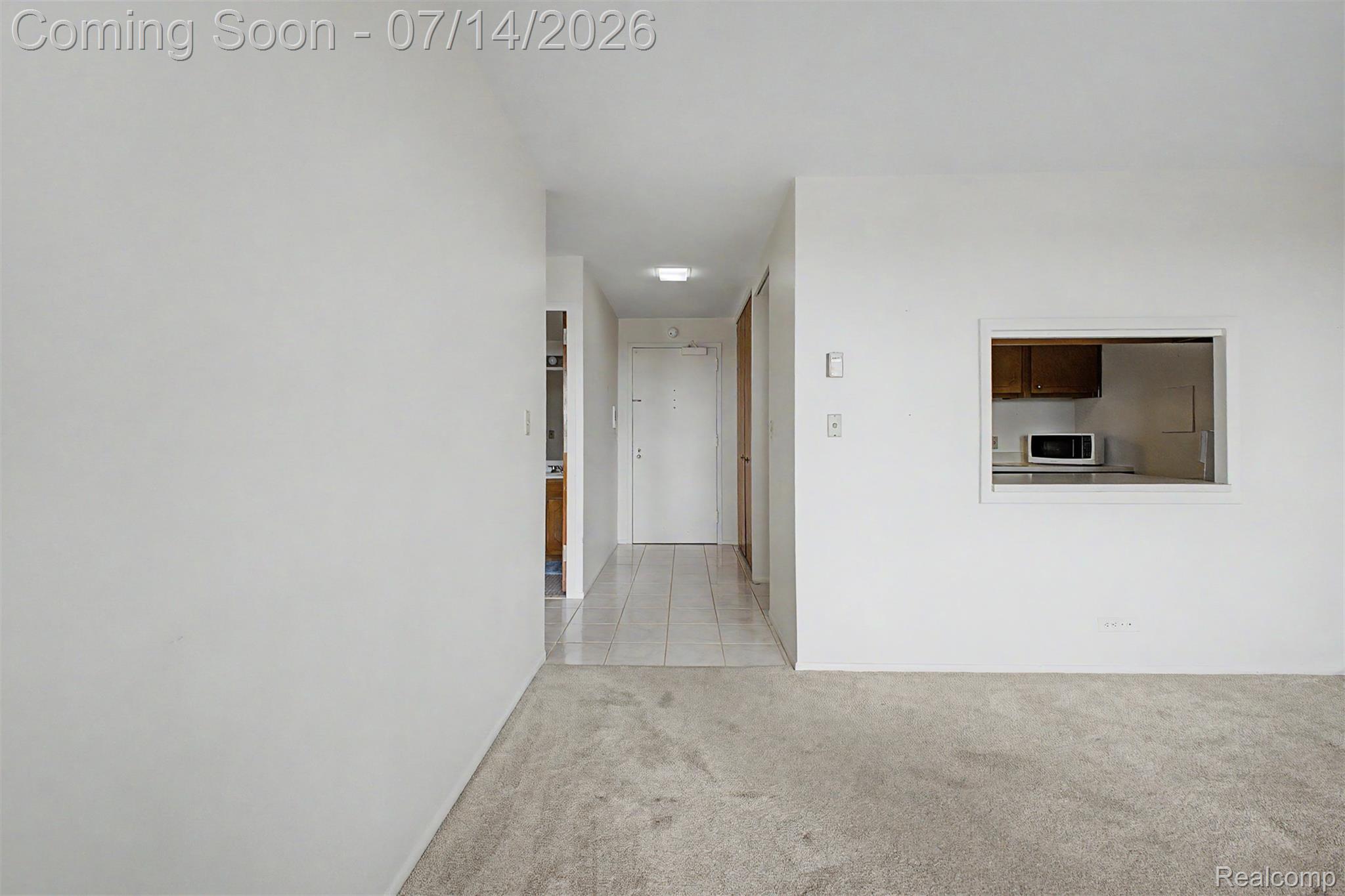 22700 Garrison Street, Unit 707 Dearborn, MI 48124 - Photo 18 of 22 Carpeted living area with a pass-through window to the kitchen, light-toned walls, and overhead lighting