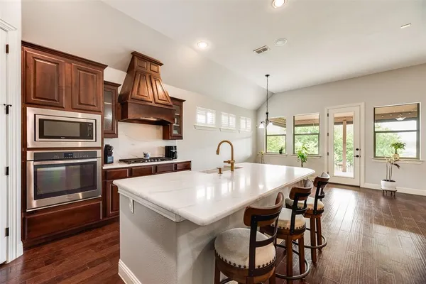 a kitchen with stainless steel appliances granite countertop a kitchen island a stove a refrigerator a dining table and chairs with wooden floor