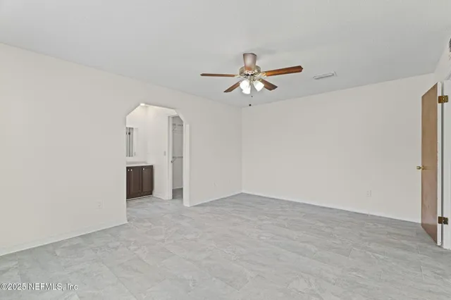 an empty room with chandelier fan and windows