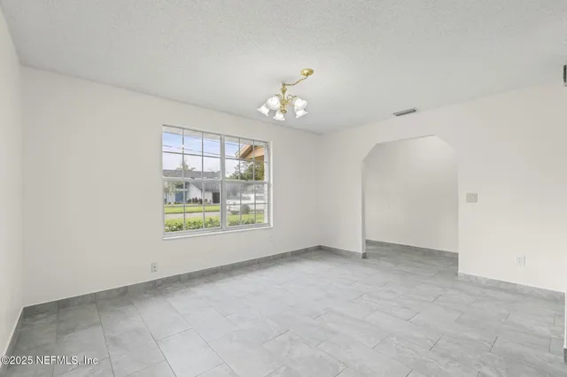 an empty room with chandelier fan and windows