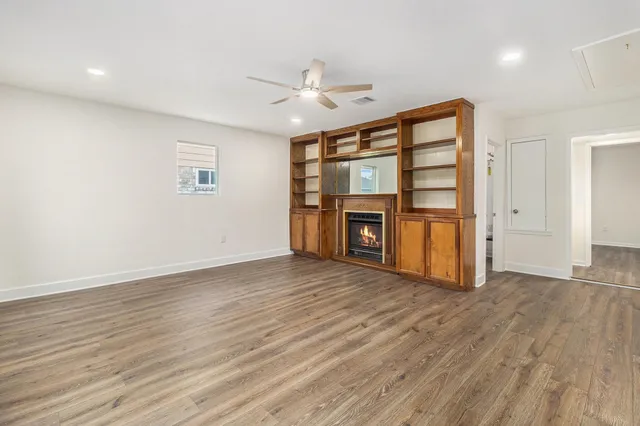 an empty room with wooden floor fireplace and windows