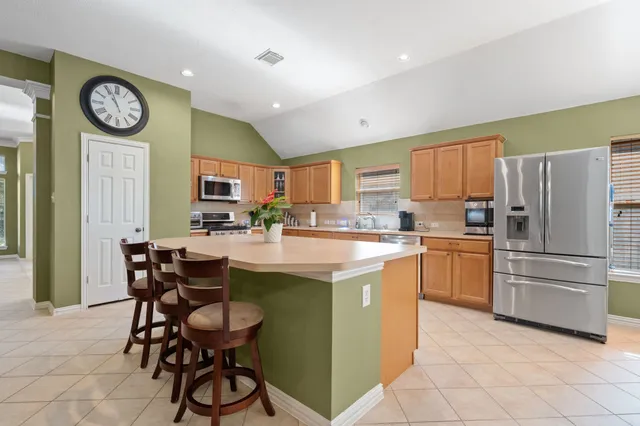 a kitchen with stainless steel appliances a stove a sink a refrigerator and chairs