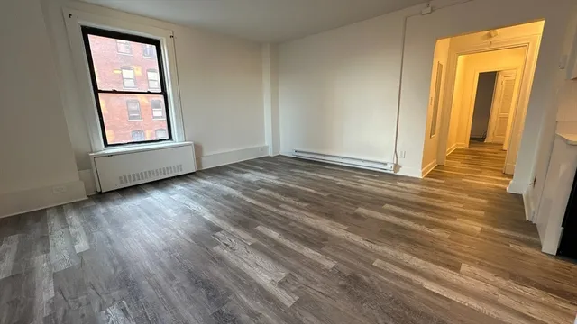 a view of an empty room with wooden floor and a window